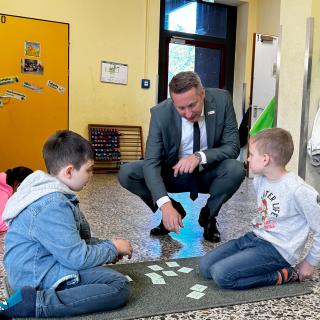 Regierungspräsident Thomas Schürmann fragt zwei Schüler der Grundschule am Dichterviertel, wie sie gemeinsam mit den Aufgaben auf den Karten Addieren lernen. Bei solchen Tandem-Übungen müssen die Kinder nicht im Klassenraum bleiben, sondern wählen ihren Ort zum Lernen selbst